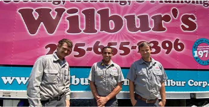 Three Wilbur’s Air Conditioning, Heating & Plumbing standing together and smiling in front of large service truck.